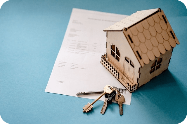 Wooden model house and keys placed on a real estate document, symbolizing property ownership or rental agreement.