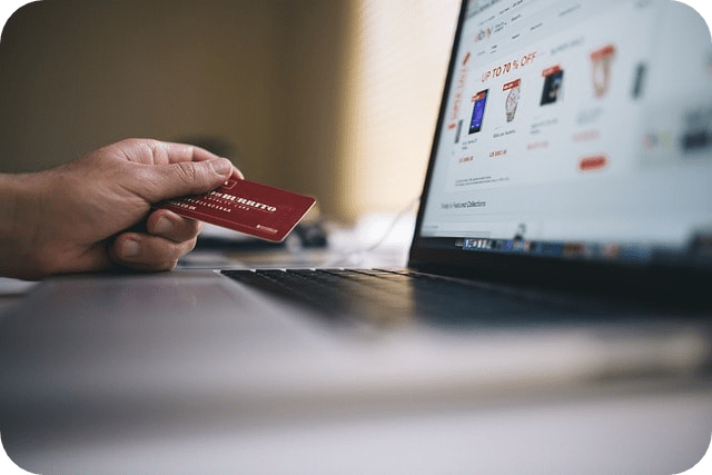 A person holding a credit card while browsing an e-commerce website on a laptop.