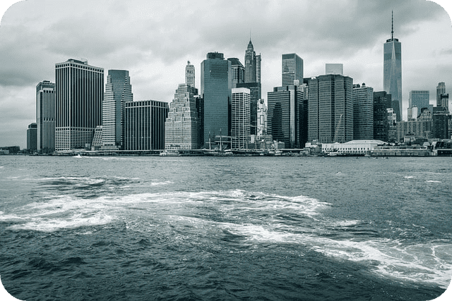A view of New York City's skyline with modern skyscrapers rising along the waterfront under a cloudy sky.
